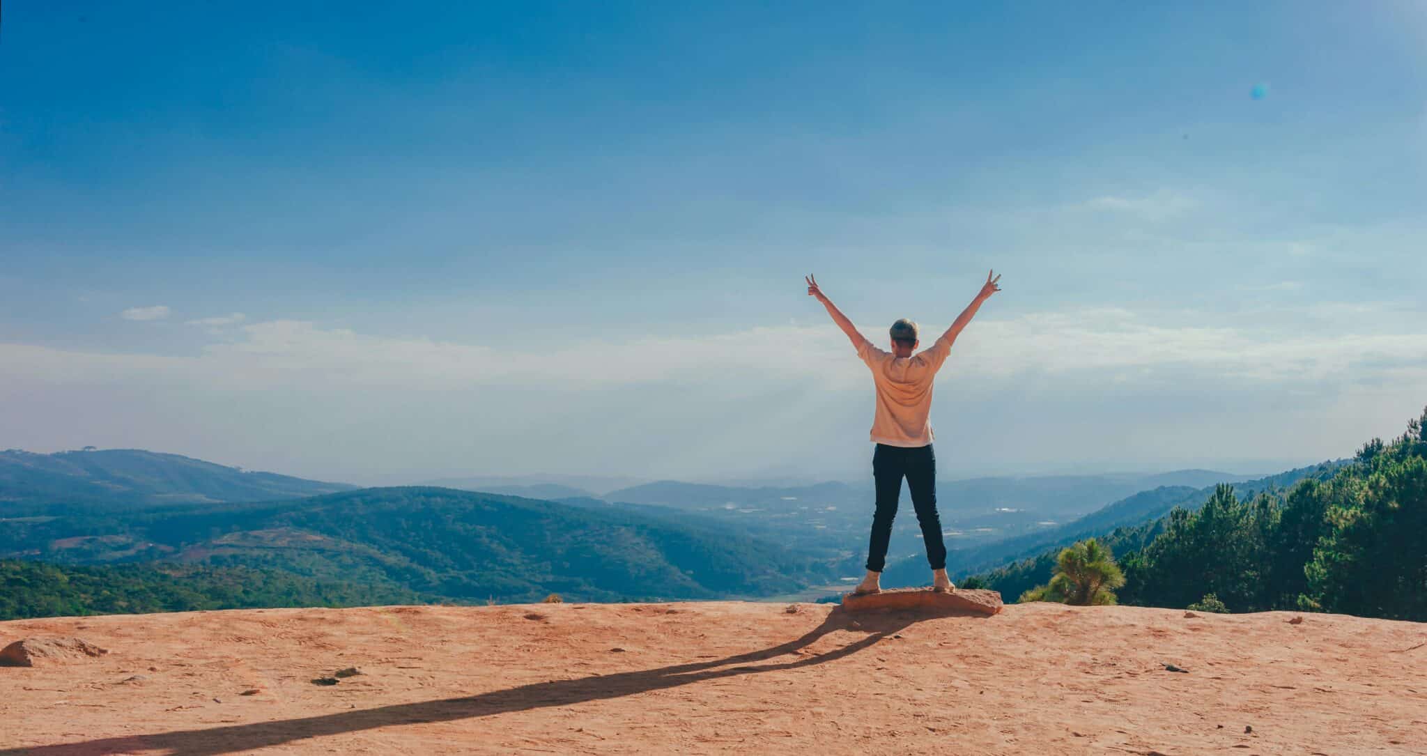 Person standing on the edge of mountain with arms raised. Food cravings.
