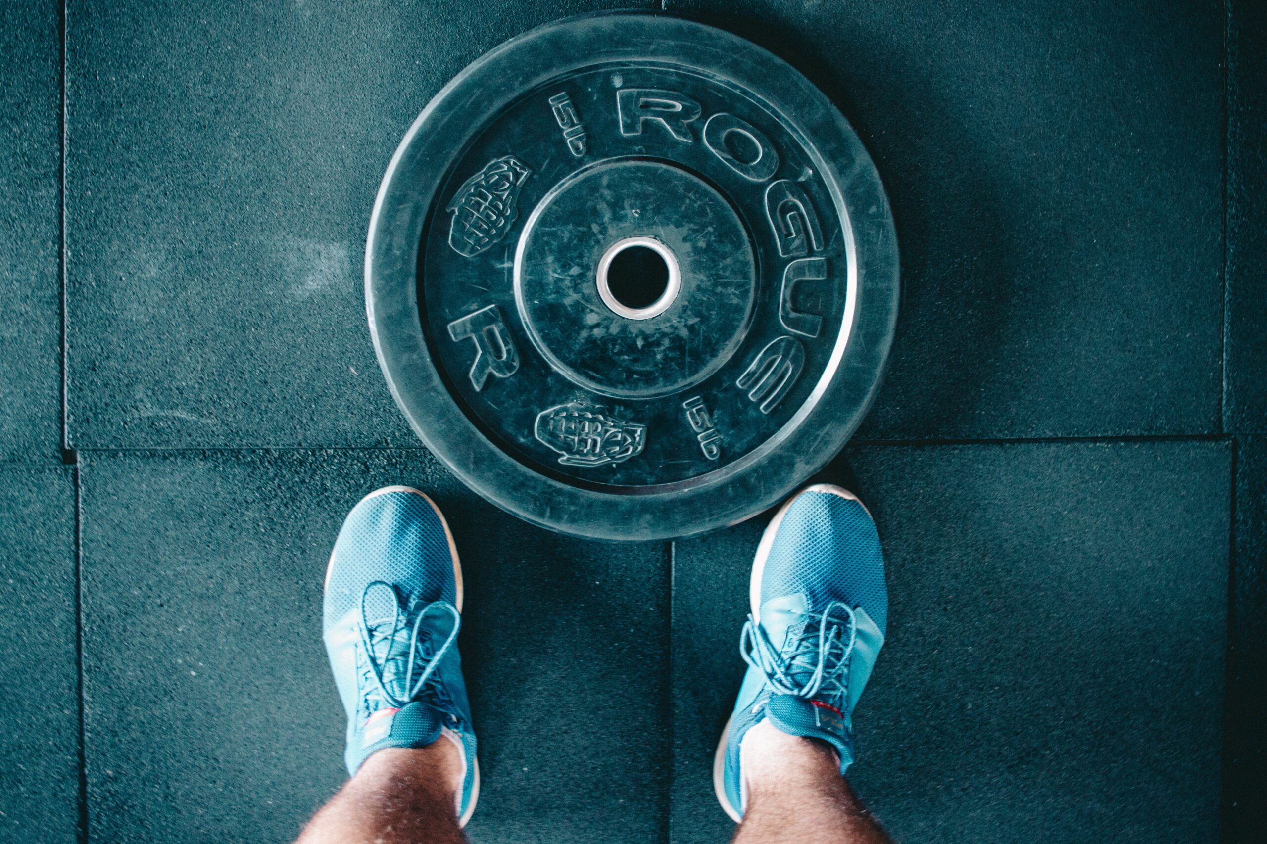 man's legs stand next to weight plate against a gym floor